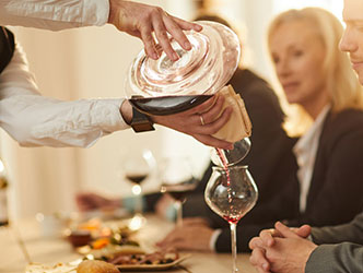 A man pouring red wine into a glass for a small group of friends doing a wine tasting