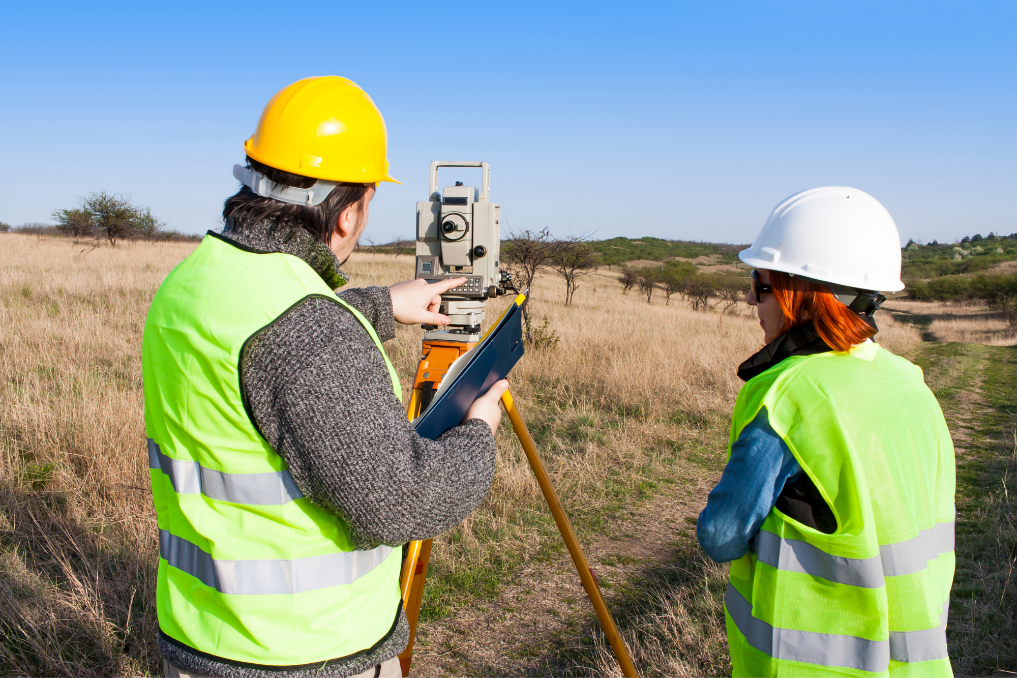 two land surveyors using equipment to survey untouched land on a sunny day
